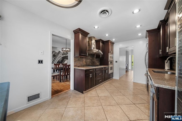 kitchen with wall chimney range hood, visible vents, appliances with stainless steel finishes, tasteful backsplash, and a sink