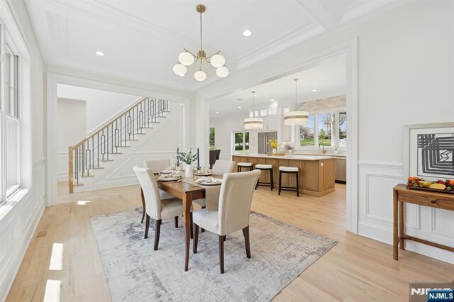 dining room with light wood-style floors, stairs, a decorative wall, and a chandelier