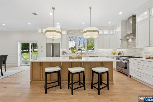 kitchen with light countertops, wall chimney exhaust hood, a center island, premium appliances, and visible vents