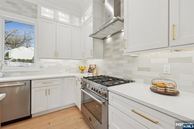 kitchen featuring appliances with stainless steel finishes, light countertops, wall chimney exhaust hood, white cabinetry, and decorative backsplash