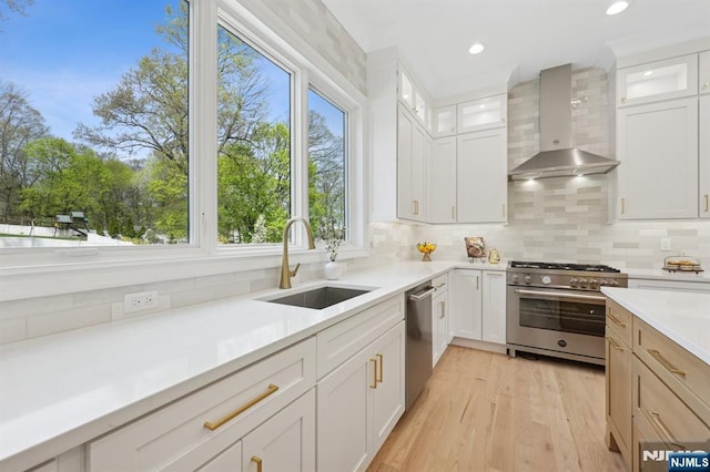 kitchen featuring wall chimney range hood, a sink, light countertops, stainless steel appliances, and backsplash