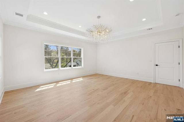 spare room featuring light wood-style floors, a chandelier, a tray ceiling, and visible vents