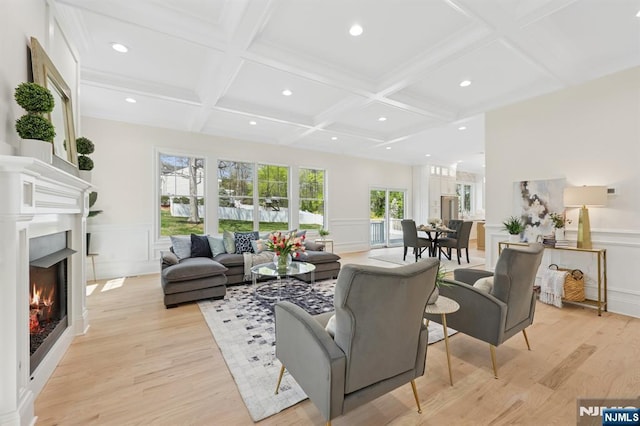 living room with a decorative wall, beamed ceiling, light wood-style floors, a lit fireplace, and coffered ceiling
