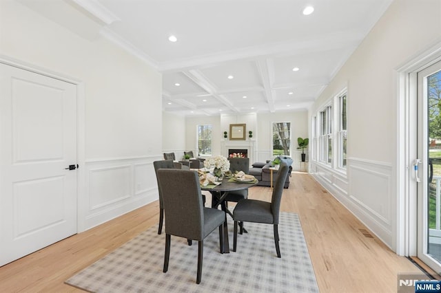 dining space with a decorative wall, beamed ceiling, coffered ceiling, and light wood-style floors