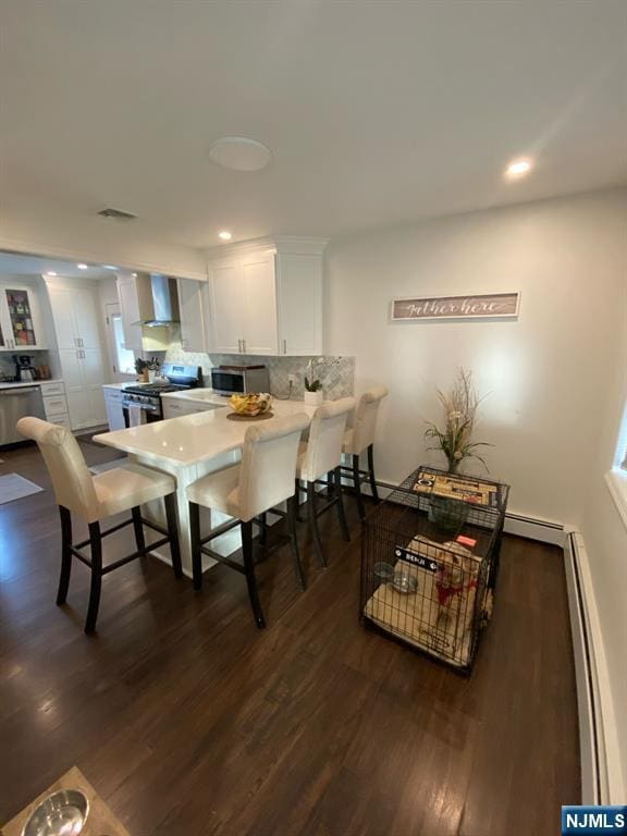 66 Lexington Ave, Rochelle Park, NJ 07662 - kitchen featuring baseboard heating, dark wood-style flooring, wall chimney exhaust hood, stainless steel appliances, and white cabinets