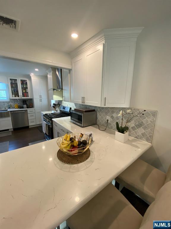 66 Lexington Ave, Rochelle Park, NJ 07662 - kitchen featuring wall chimney range hood, stainless steel appliances, white cabinets, and visible vents