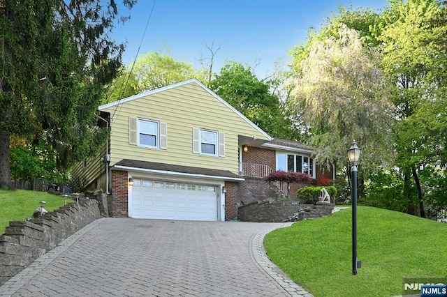 split level home featuring brick siding, decorative driveway, a front lawn, and an attached garage