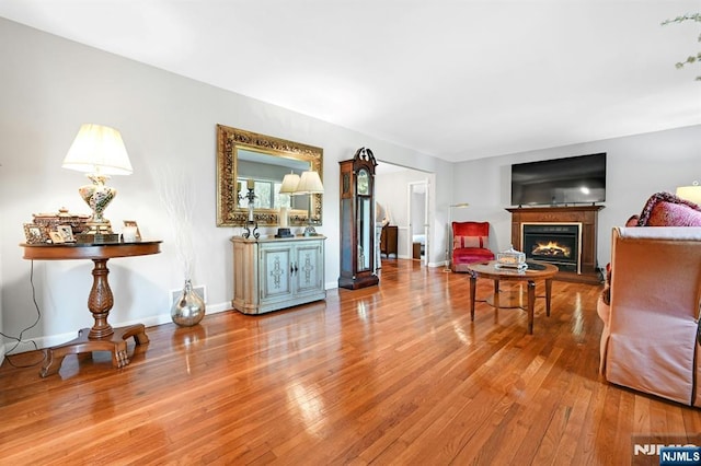 living room with baseboards, a lit fireplace, hardwood / wood-style floors, and visible vents