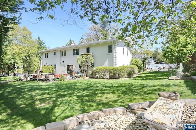 back of property with a lawn, stucco siding, and a chimney