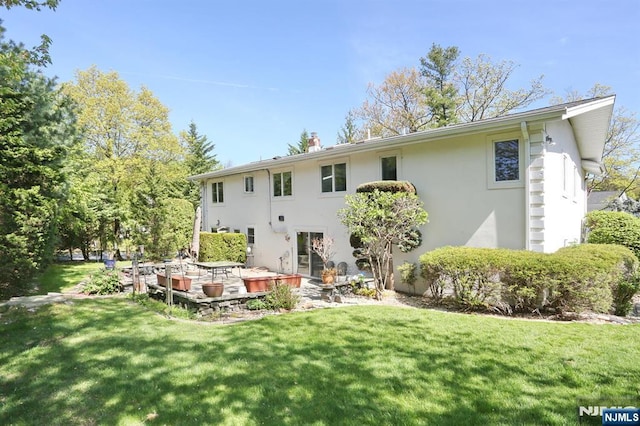 back of property featuring a patio, stucco siding, a yard, and a chimney