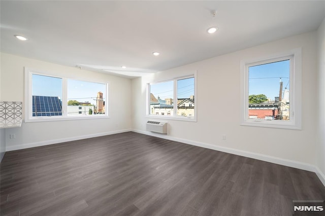 empty room with baseboards, dark wood-style flooring, a wall mounted air conditioner, and a wealth of natural light