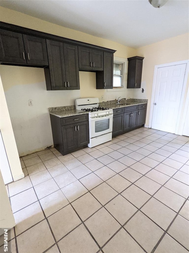 kitchen featuring a sink, light tile patterned floors, dark cabinets, and white range with gas cooktop