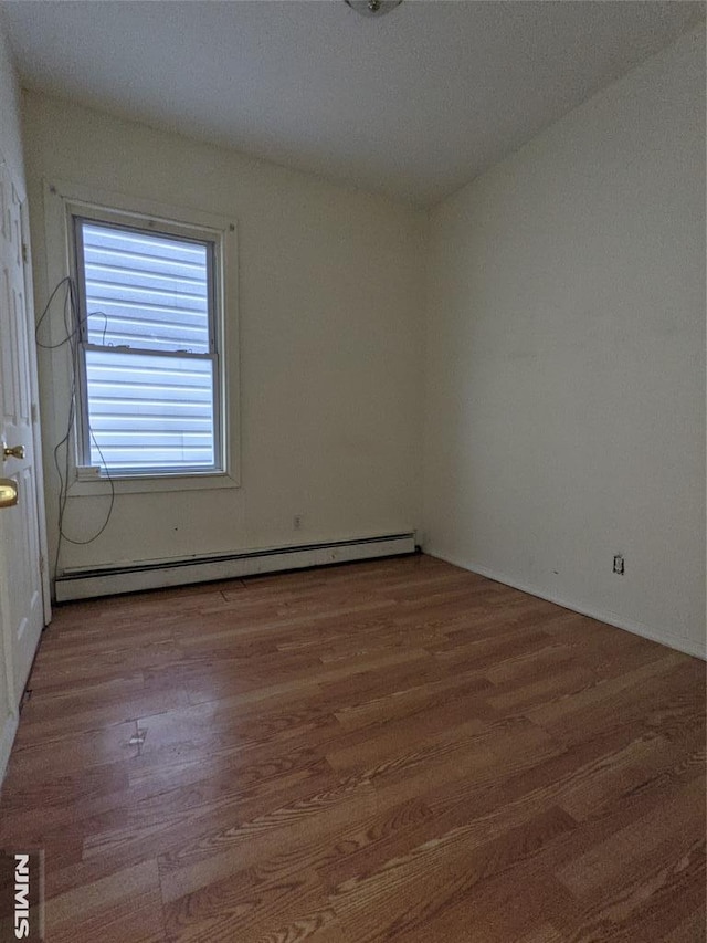 unfurnished room featuring wood finished floors and a baseboard radiator