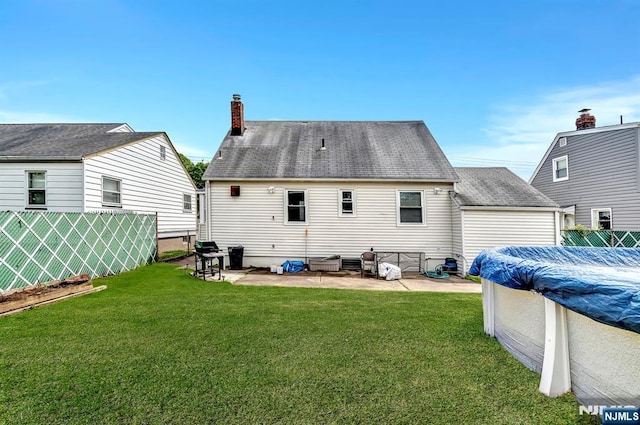 back of house with fence, a chimney, a covered pool, a patio area, and a yard