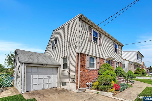 view of side of property featuring brick siding, an attached garage, fence, and concrete driveway