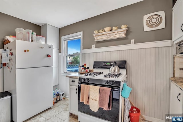 kitchen featuring gas range, light countertops, a wainscoted wall, white cabinets, and freestanding refrigerator