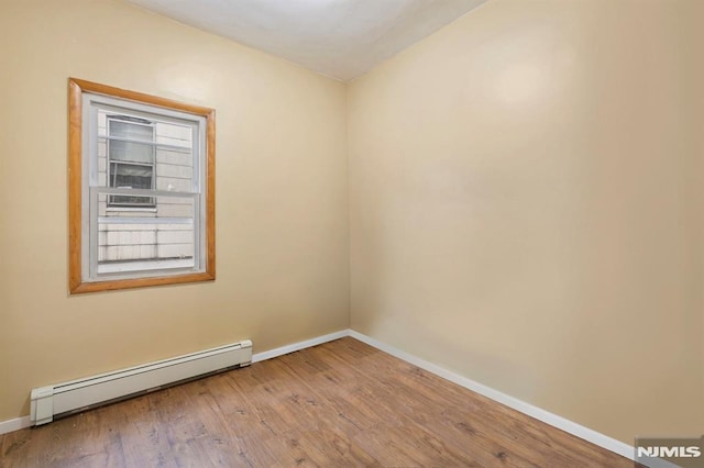 spare room with baseboards, a baseboard heating unit, and wood finished floors