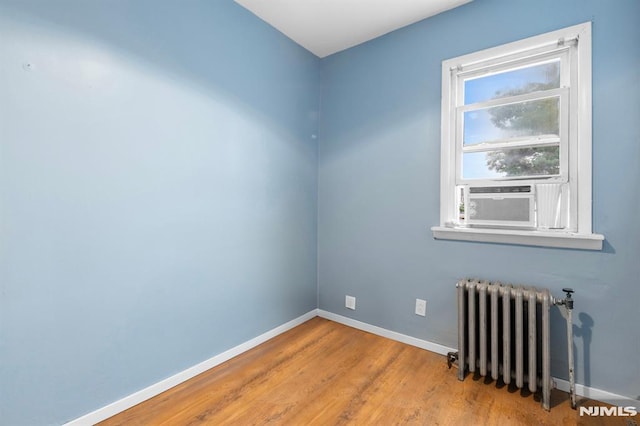 empty room featuring baseboards, radiator, wood finished floors, and cooling unit