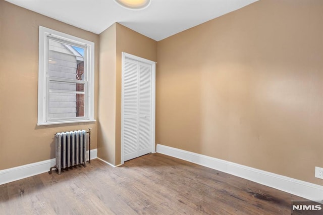 unfurnished bedroom with wood finished floors, baseboards, radiator heating unit, and a closet