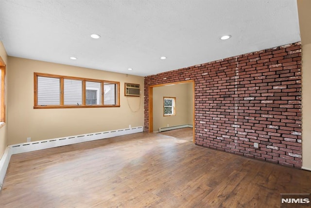 empty room with brick wall, a baseboard heating unit, a wall unit AC, and wood finished floors