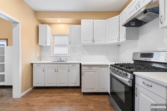 kitchen featuring decorative backsplash, stainless steel gas range oven, white cabinetry, under cabinet range hood, and a sink