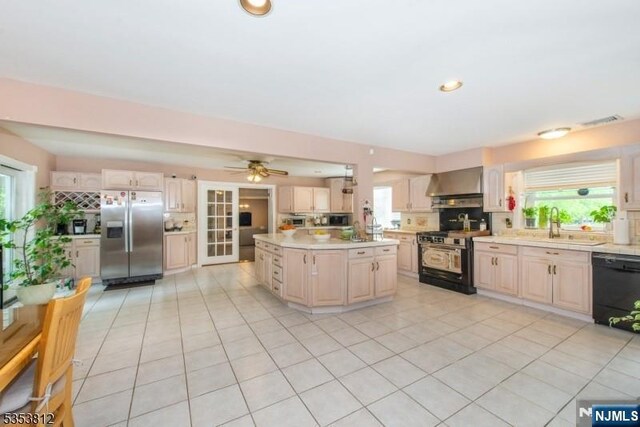 kitchen featuring appliances with stainless steel finishes, a sink, light countertops, wall chimney exhaust hood, and light tile patterned floors