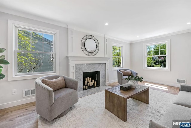 living room featuring visible vents, crown molding, wood finished floors, baseboards, and a high end fireplace