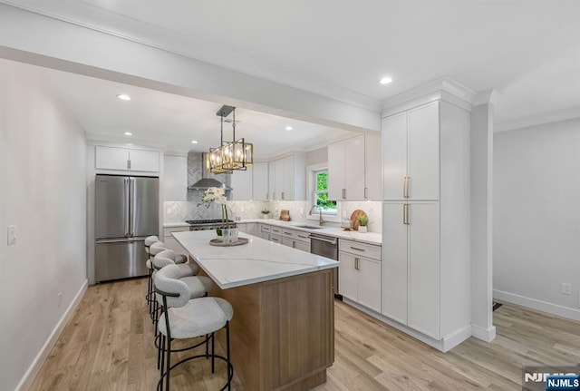 kitchen featuring decorative backsplash, a kitchen island, wall chimney range hood, light wood-style flooring, and stainless steel appliances