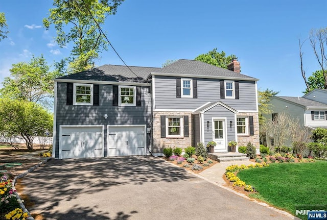 view of front of house featuring a garage, stone siding, a front yard, a chimney, and driveway
