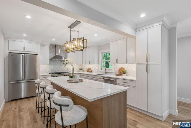 kitchen with wall chimney range hood, appliances with stainless steel finishes, a sink, light wood-style flooring, and ornamental molding