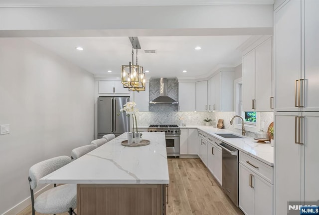 kitchen with a kitchen island, high quality appliances, wall chimney exhaust hood, a sink, and light wood finished floors