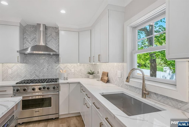 kitchen with wall chimney exhaust hood, stainless steel range, white cabinets, a sink, and backsplash