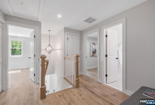 corridor with light wood-style floors, baseboards, visible vents, and an upstairs landing