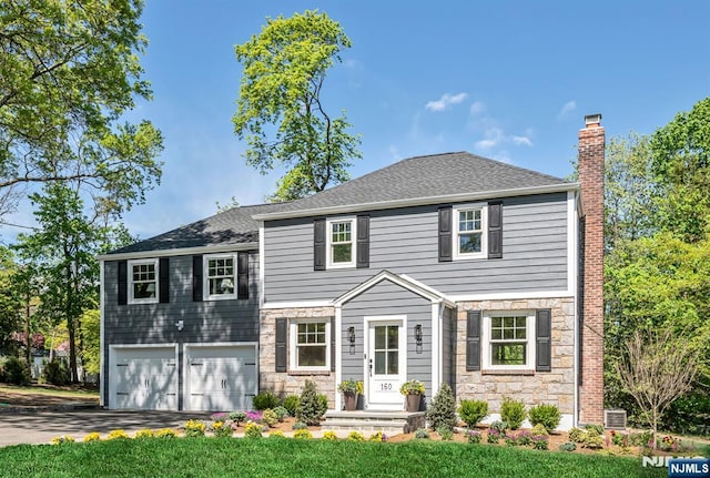 tri-level home featuring an attached garage, a chimney, stone siding, and aphalt driveway