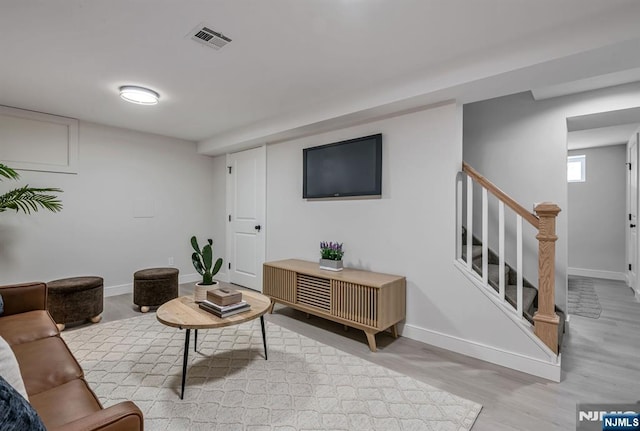 living area with stairway, baseboards, light wood-style flooring, and visible vents