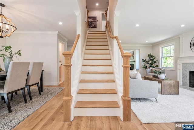stairs with crown molding, recessed lighting, wood finished floors, and a chandelier