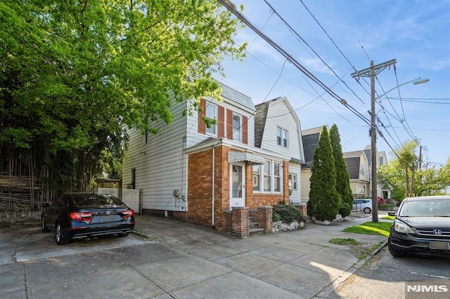 118 W 49th St, Bayonne, NJ 07002 - view of side of property with brick siding, a gambrel roof, uncovered parking, and fence