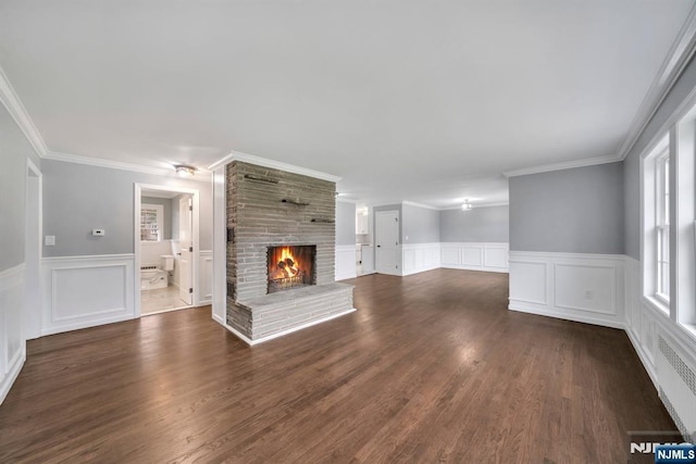 unfurnished living room with crown molding, a decorative wall, a fireplace, and wainscoting
