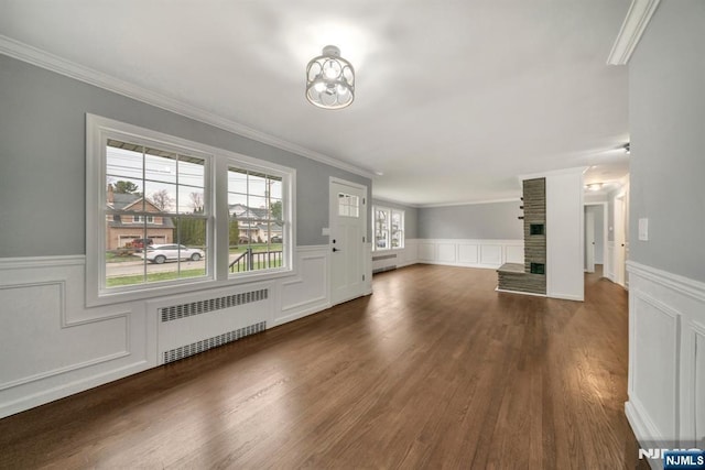 unfurnished living room featuring a brick fireplace, wood finished floors, radiator heating unit, and a decorative wall