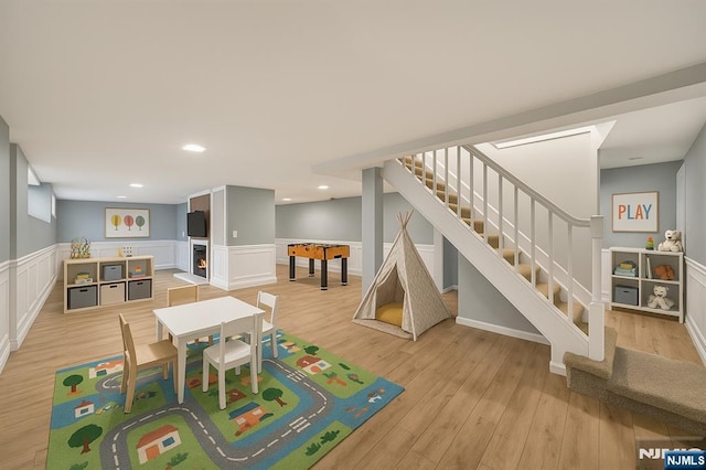 recreation room featuring recessed lighting, light wood finished floors, a decorative wall, and a wainscoted wall
