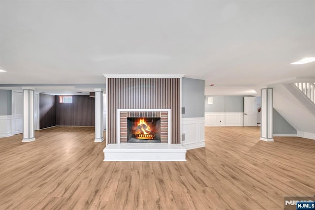 unfurnished living room with a brick fireplace, light wood-type flooring, stairway, and a decorative wall
