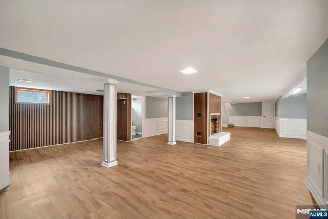 below grade area featuring wainscoting, light wood-type flooring, a brick fireplace, a decorative wall, and stairs