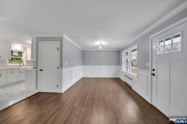 entrance foyer featuring crown molding, dark wood finished floors, a wainscoted wall, radiator, and a decorative wall