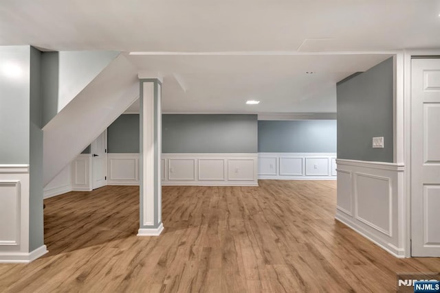 bonus room featuring wainscoting, a decorative wall, and light wood-type flooring