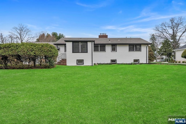 back of property with a shingled roof, a yard, and a chimney