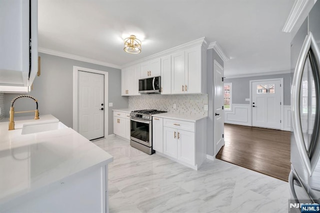 kitchen featuring white cabinetry, appliances with stainless steel finishes, ornamental molding, and a sink
