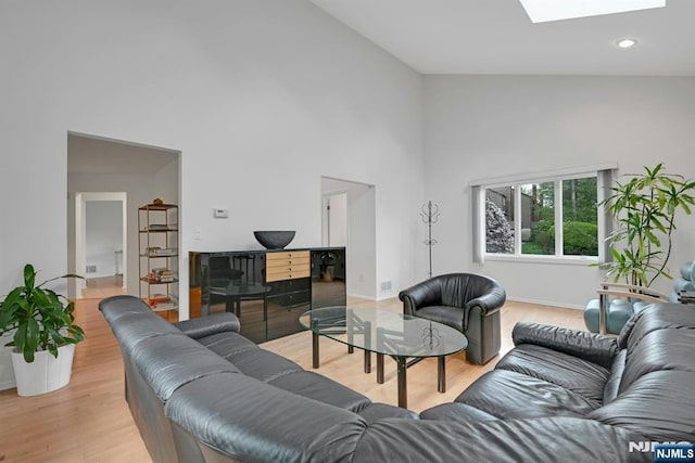 living area with a skylight, high vaulted ceiling, baseboards, and light wood-type flooring