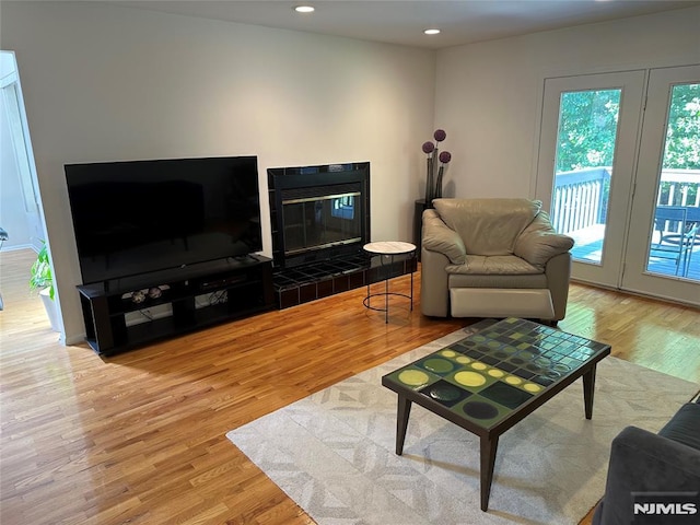 living room with recessed lighting, a tiled fireplace, and light wood-type flooring