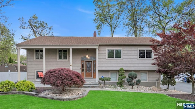 split foyer home with fence, a shingled roof, and a front lawn