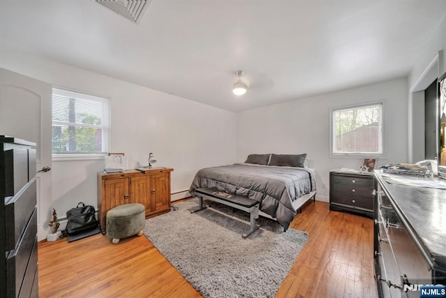 bedroom with light wood-style floors, multiple windows, baseboard heating, and visible vents